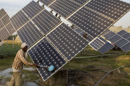 Farm workers clean the solar panels of a solar water pump at the farms of Gurinder Singh.