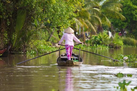 Woman steering a boat down a canal off the Hau River in Can Tho Province, Vietnam. 