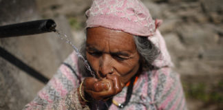 Ganesh Kumari Karki (60) drinks water from a public tap at Dhap village. Photo: Tom van Cakenberghe / IWMI